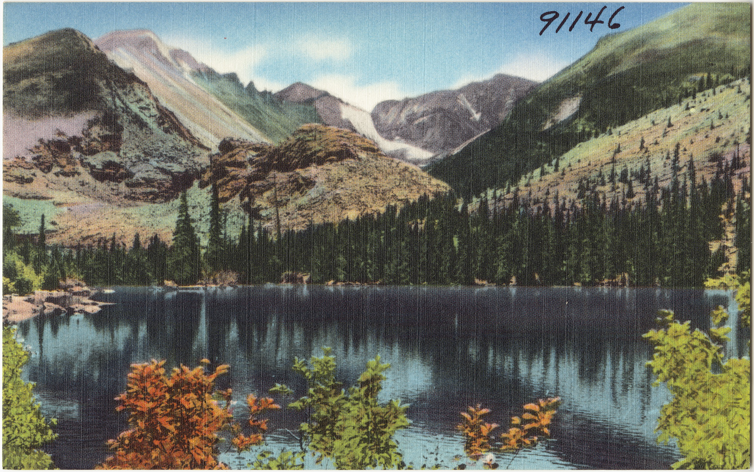 A scenic view of Bear Lake with Long's Peak and Glacier Gorge in the background, surrounded by lush forest and mountains.